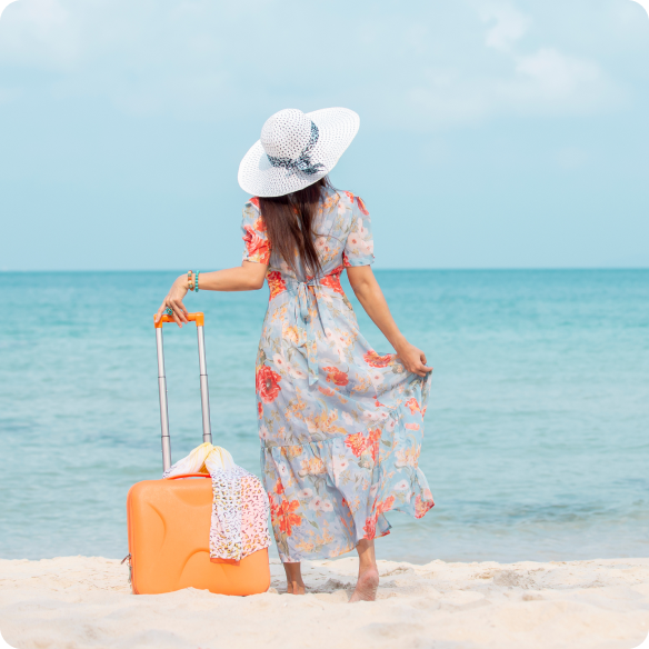 Девушка стоит на пляже с чемоданом